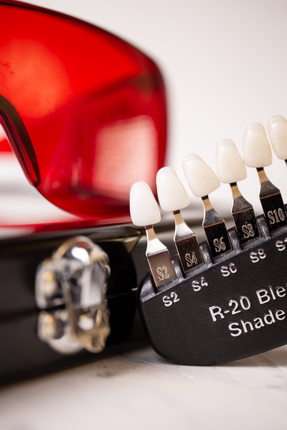 Close-up of dental shade guide showing multiple tooth shades next to red protective glasses.