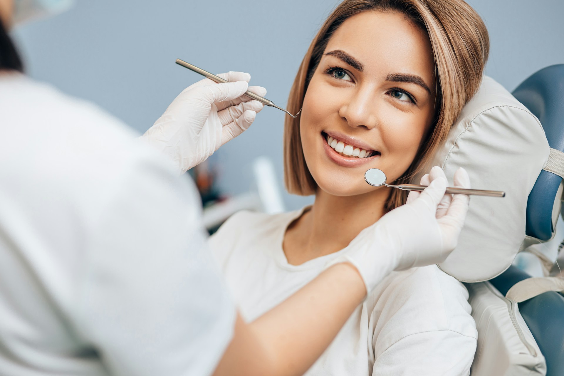 Smiling woman in a dental chair as a dentist holds a mirror and probe for her exam