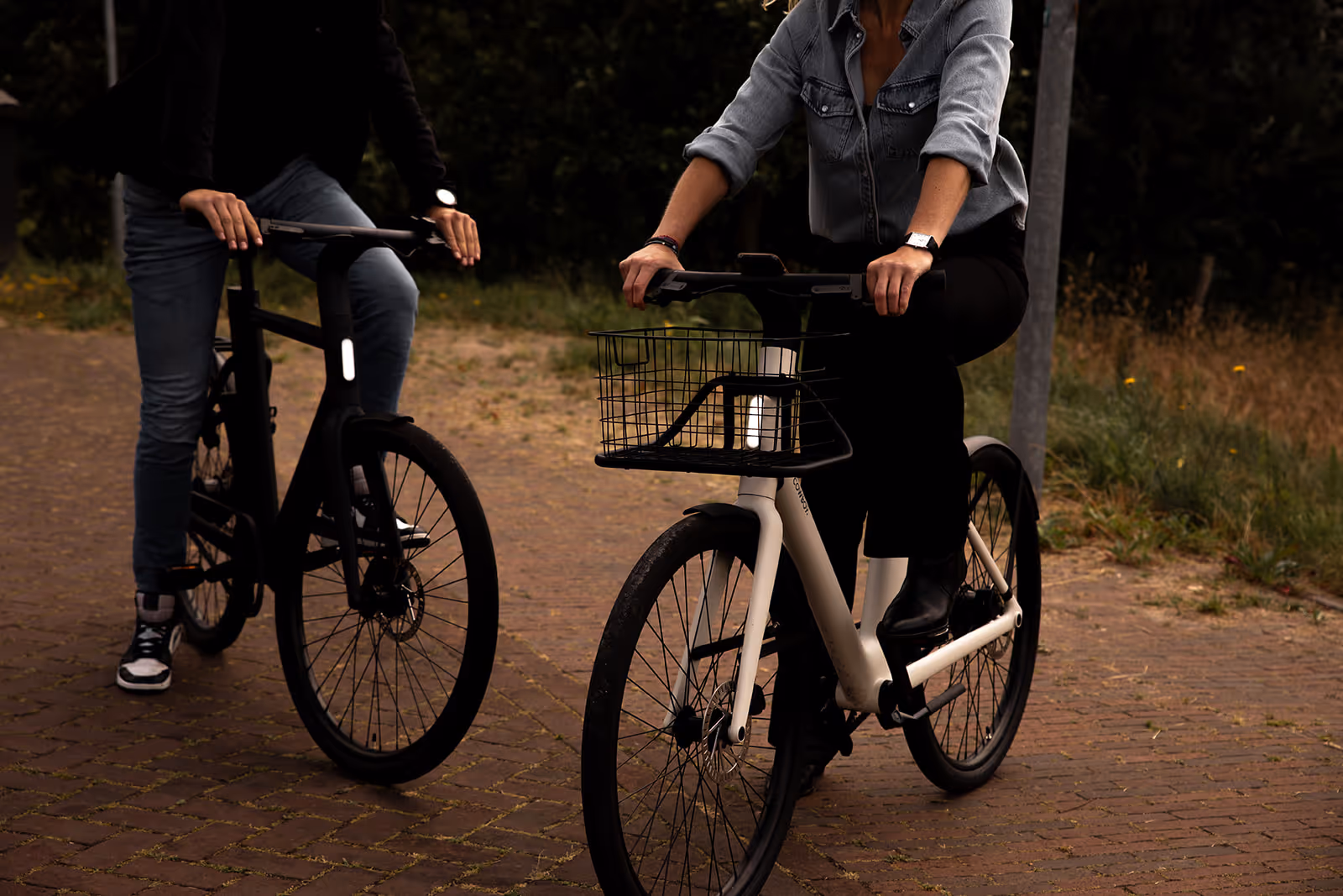 Twee personen fietsen op een pad, een vrouw op een witte fiets met een mand en een man op een zwarte fiets.