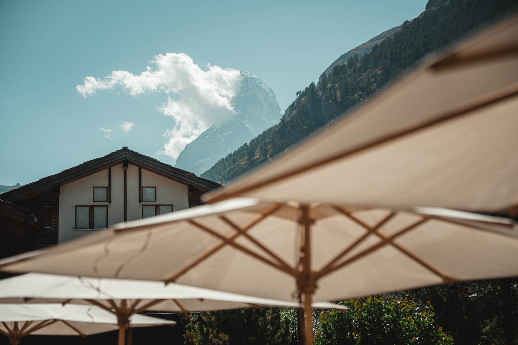Sonnige Terrasse im Alpen Resort & Spa Zermatt mit Blick auf das Matterhorn, weisse Sonnenschirme vor der imposanten Walliser Bergkulisse im Winter.