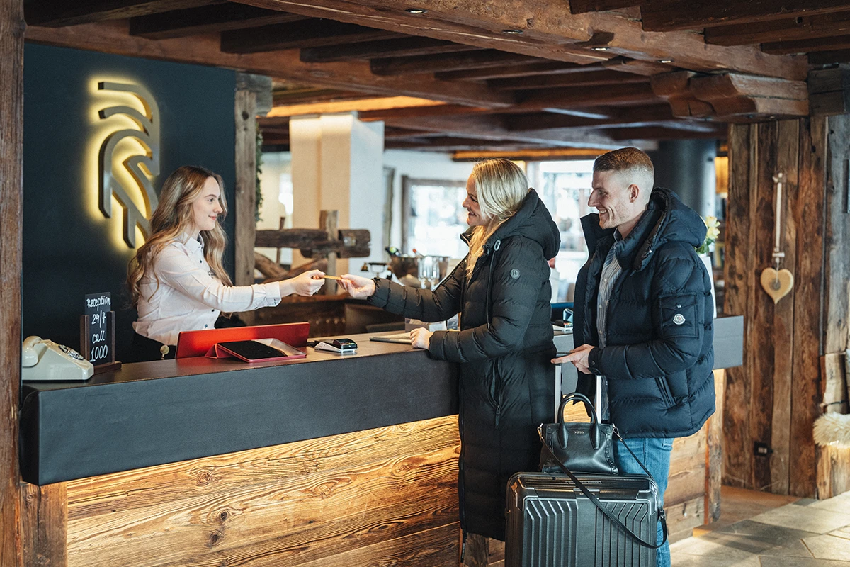 Freundlicher Empfang und Check-in im Alpen Resort Hotel und Spa in Zermatt, Gäste mit Winterjacken und Koffer in einer alpinen Unterkunft.