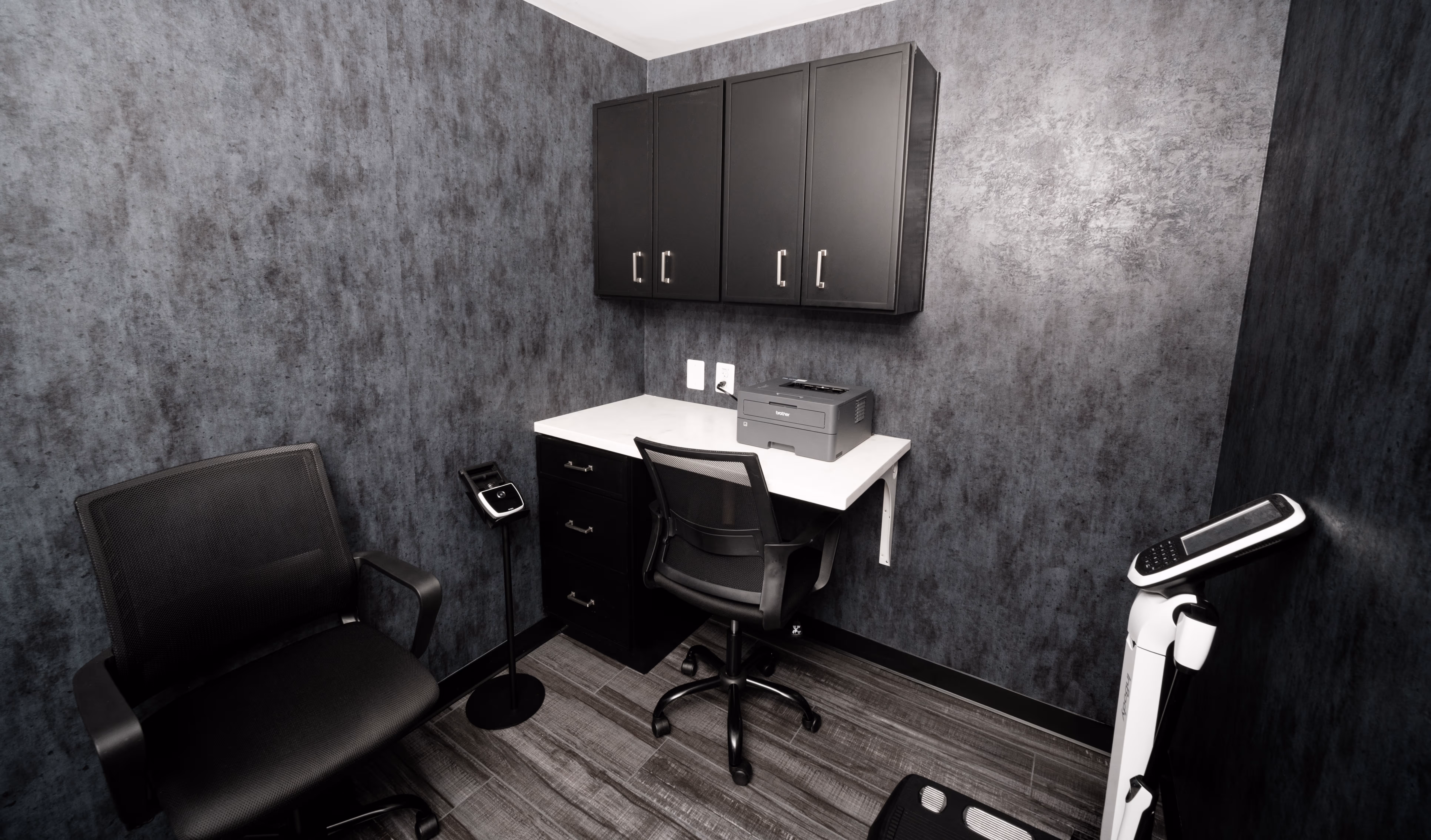 Small modern office with black mesh chairs, white desk, black cabinets, printer, and a body composition scale.