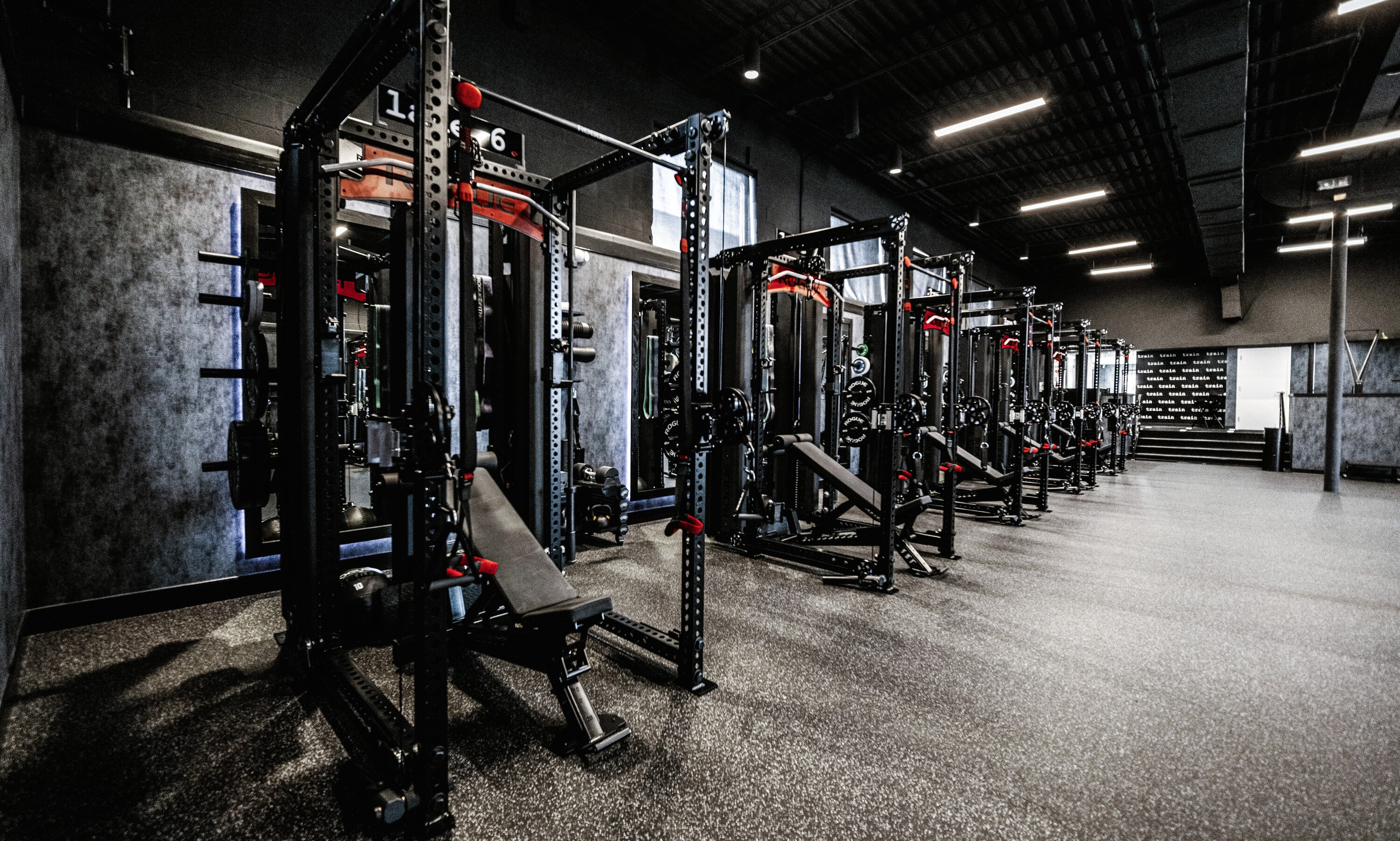 Row of black and red weight training racks with benches in a modern gym room.
