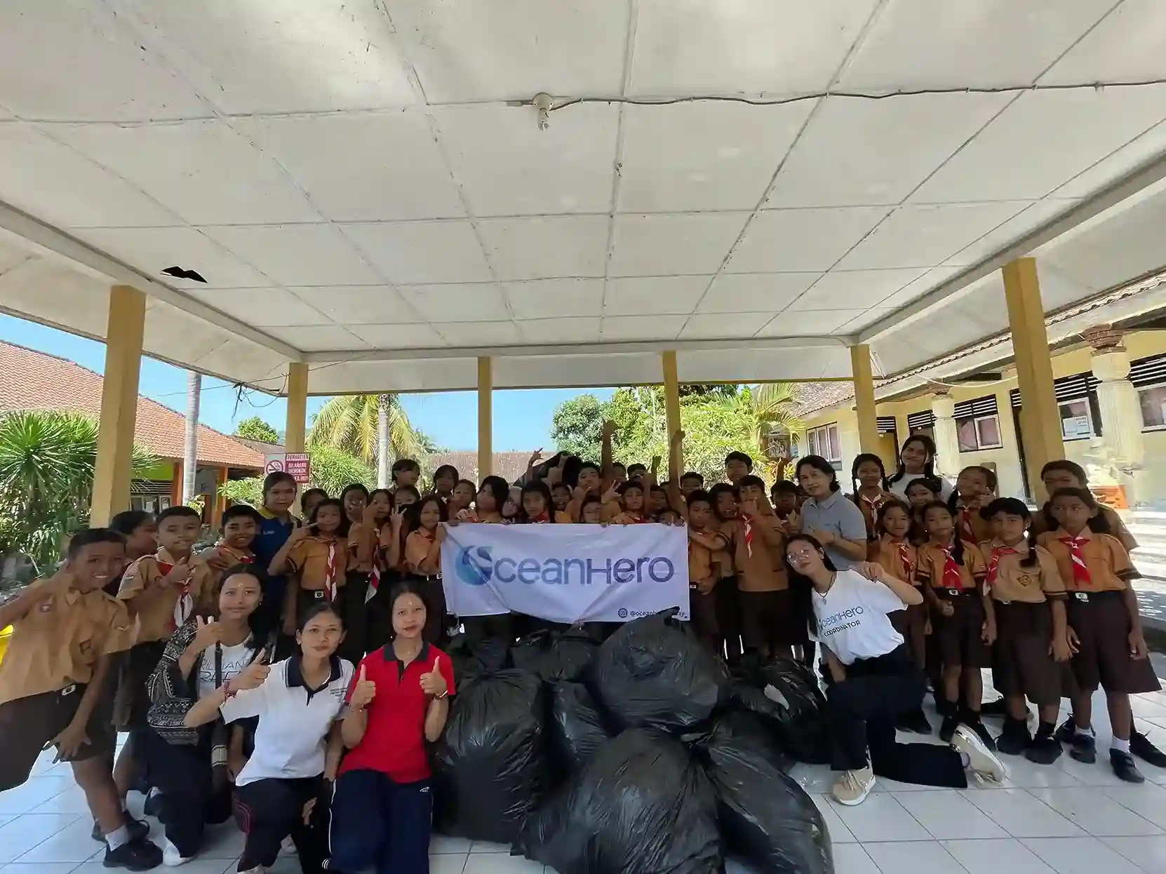 OceanHero team and students at SDN 1 Bebandem holding collected waste bags during a plastic cleanup activity