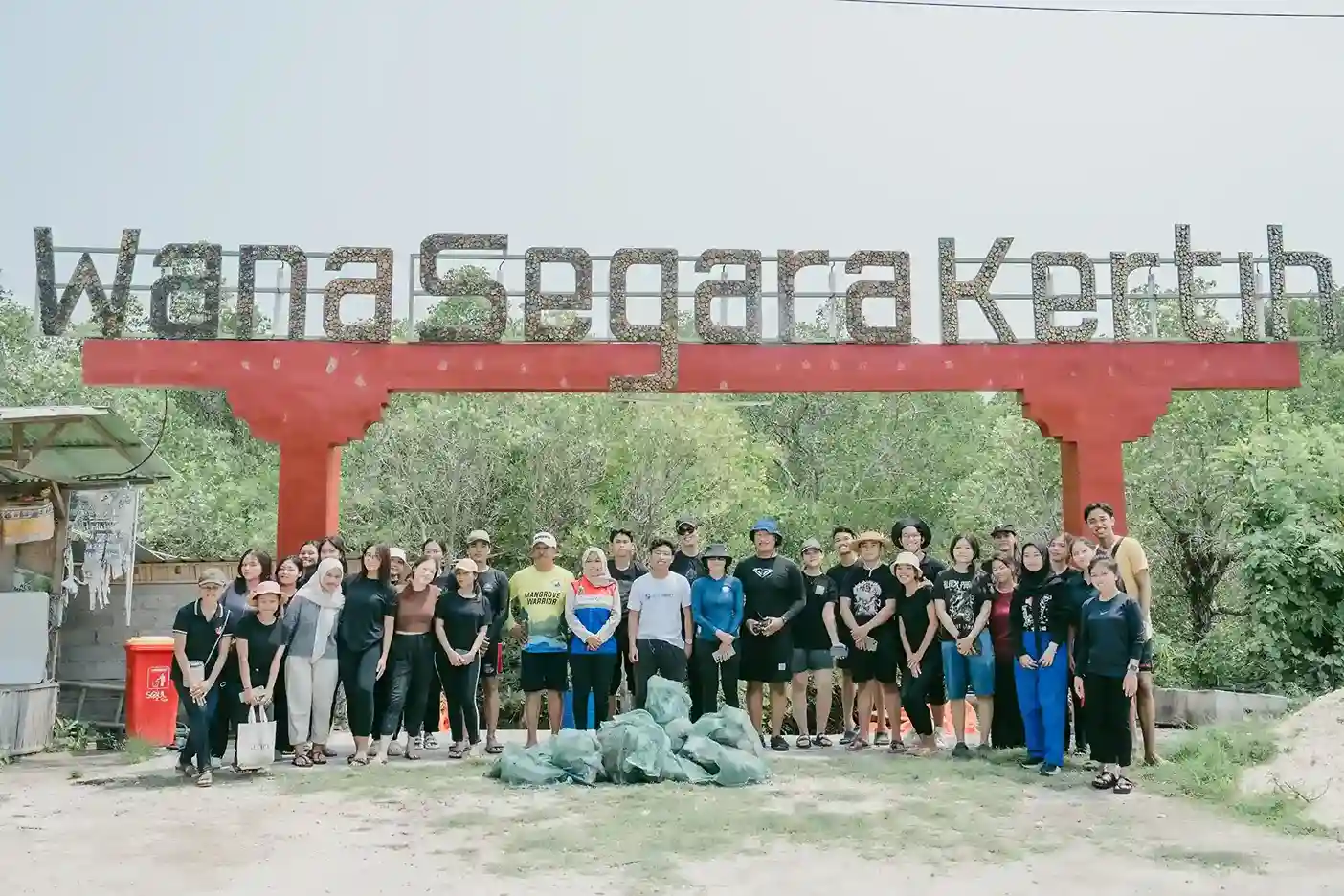Group of volunteers at Wana Segara Kertih mangrove cleanup, holding collected waste bags at the entrance gate