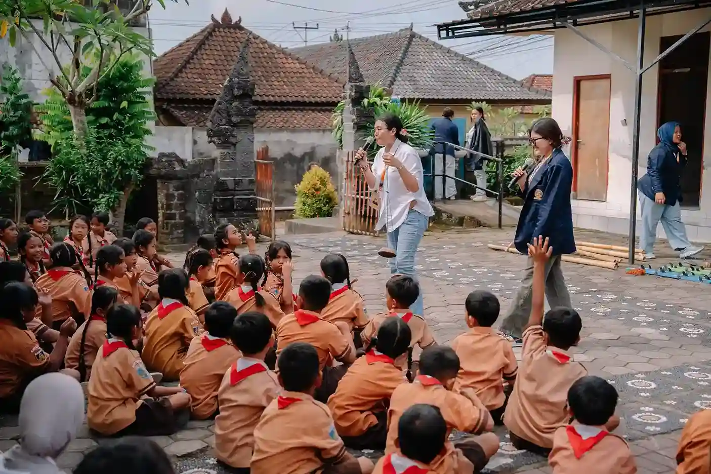 Students in orange uniforms engage in an outdoor environmental awareness activity led by young educators in Bali