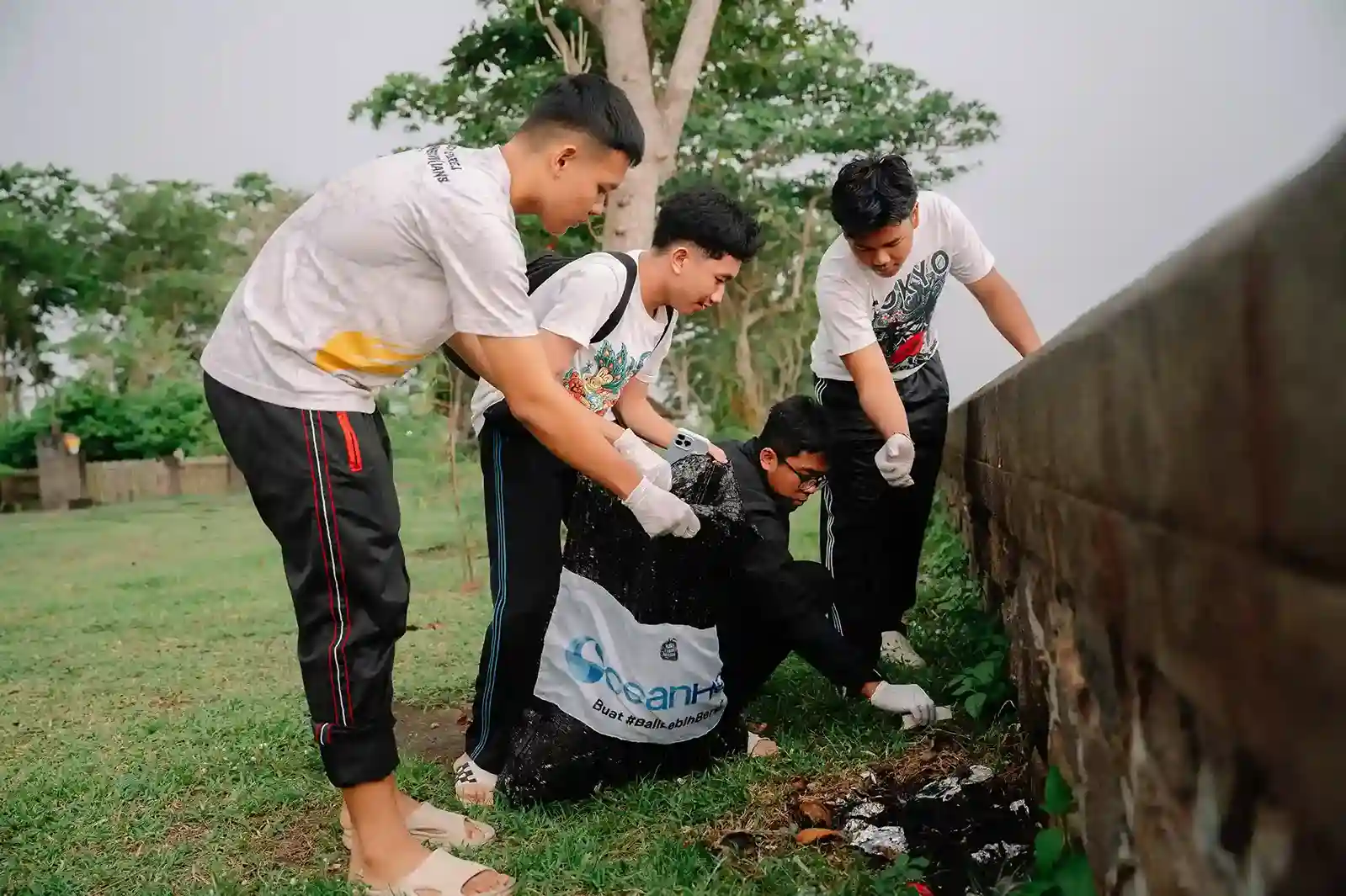 Young volunteers collecting trash in garbage bags during Dlodberawah Beach clean-up event with OceanHero