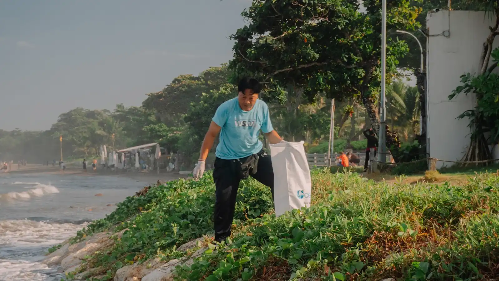 A volunteer carrying a sack along the shoreline at Double Six Beach