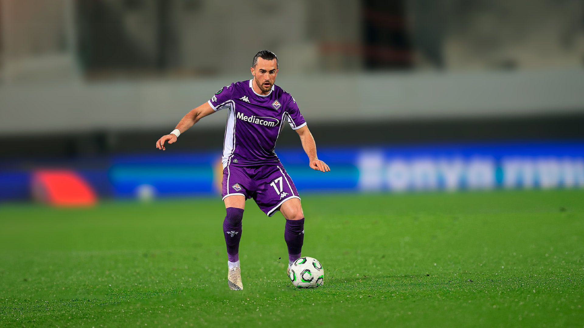 Soccer player in purple uniform controlling ball on green field during a game.
