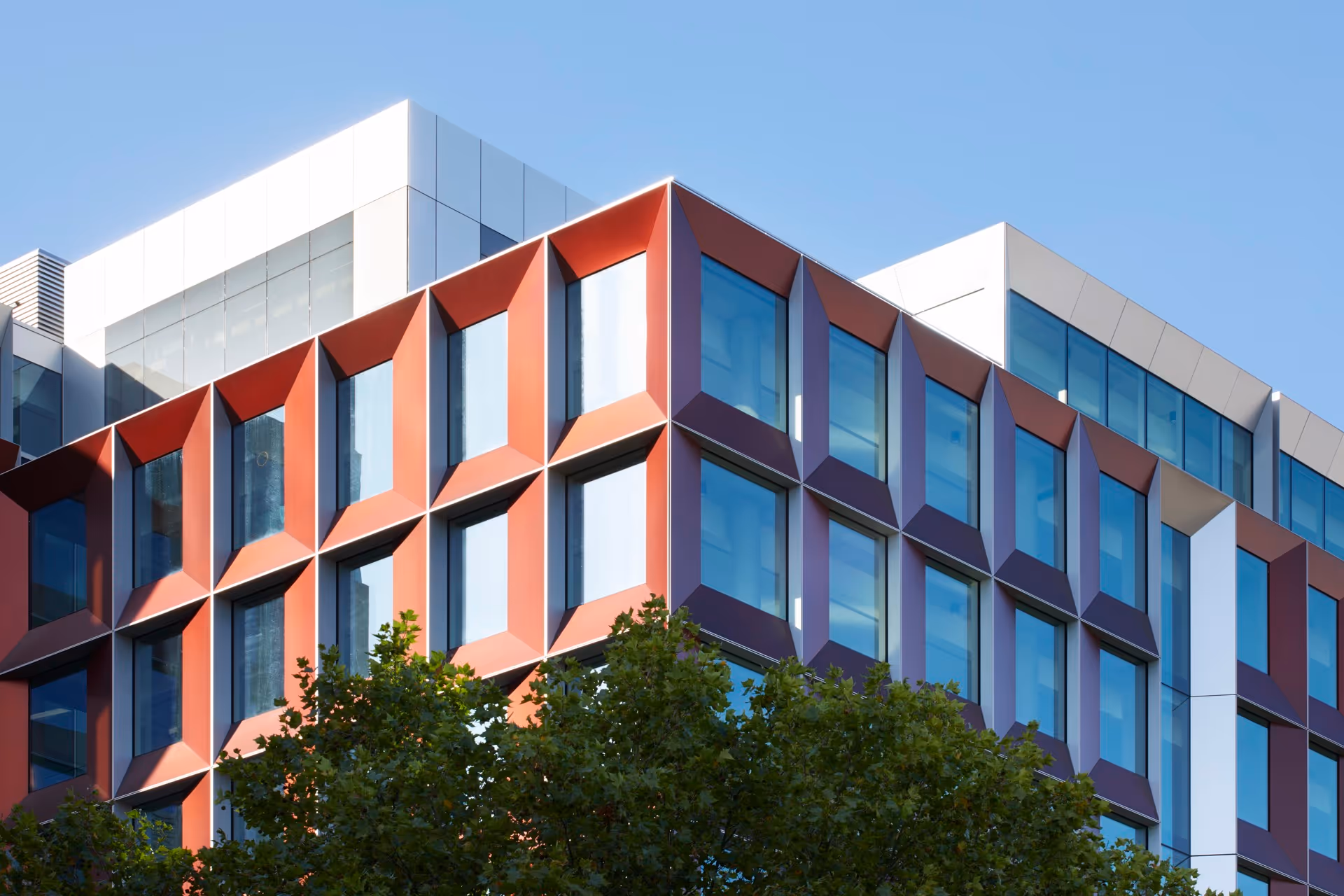 Modern office building corner with geometric orange and white window frames under a clear blue sky.