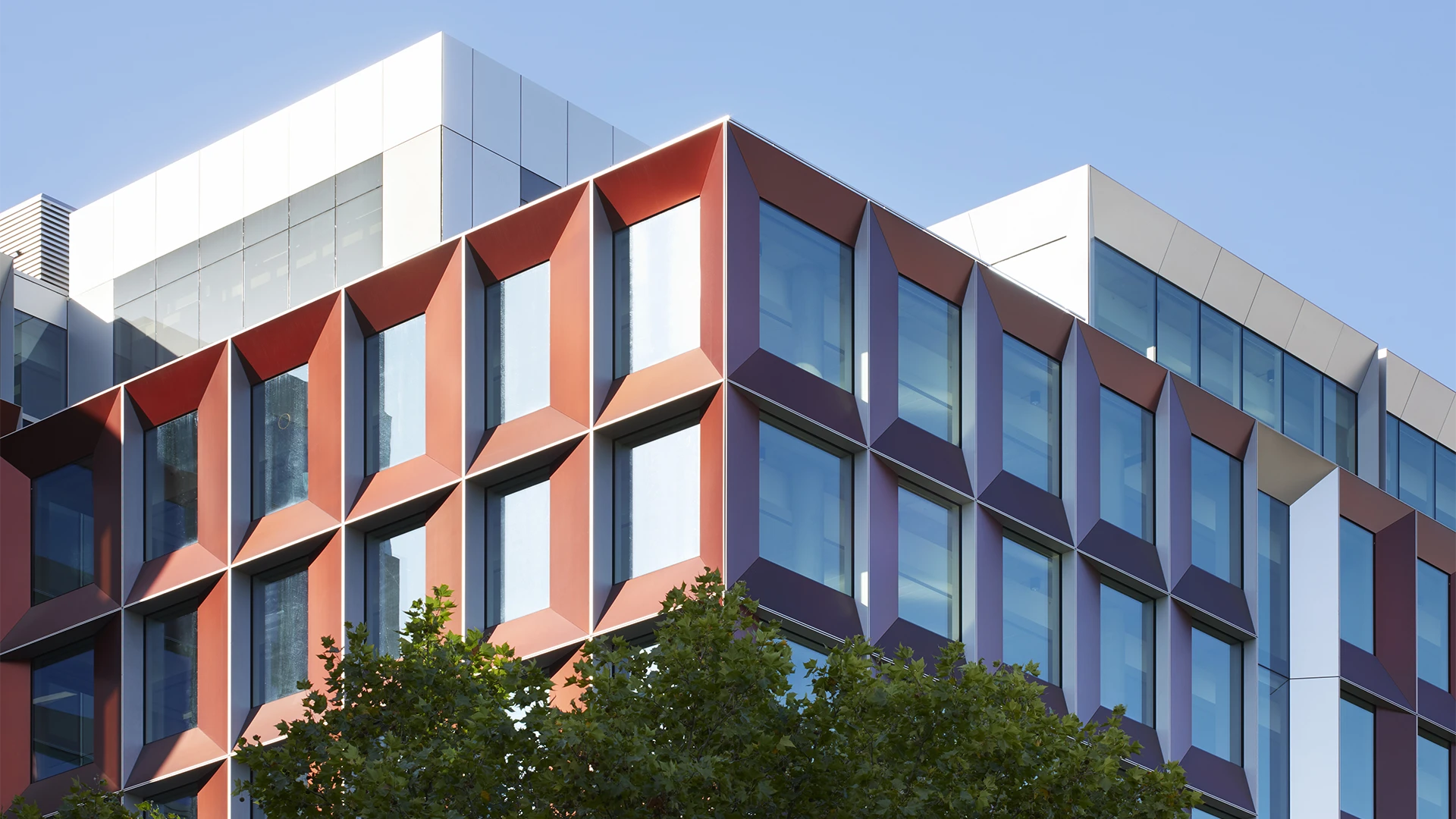 Modern office building corner with geometric orange and white window frames under a clear blue sky.