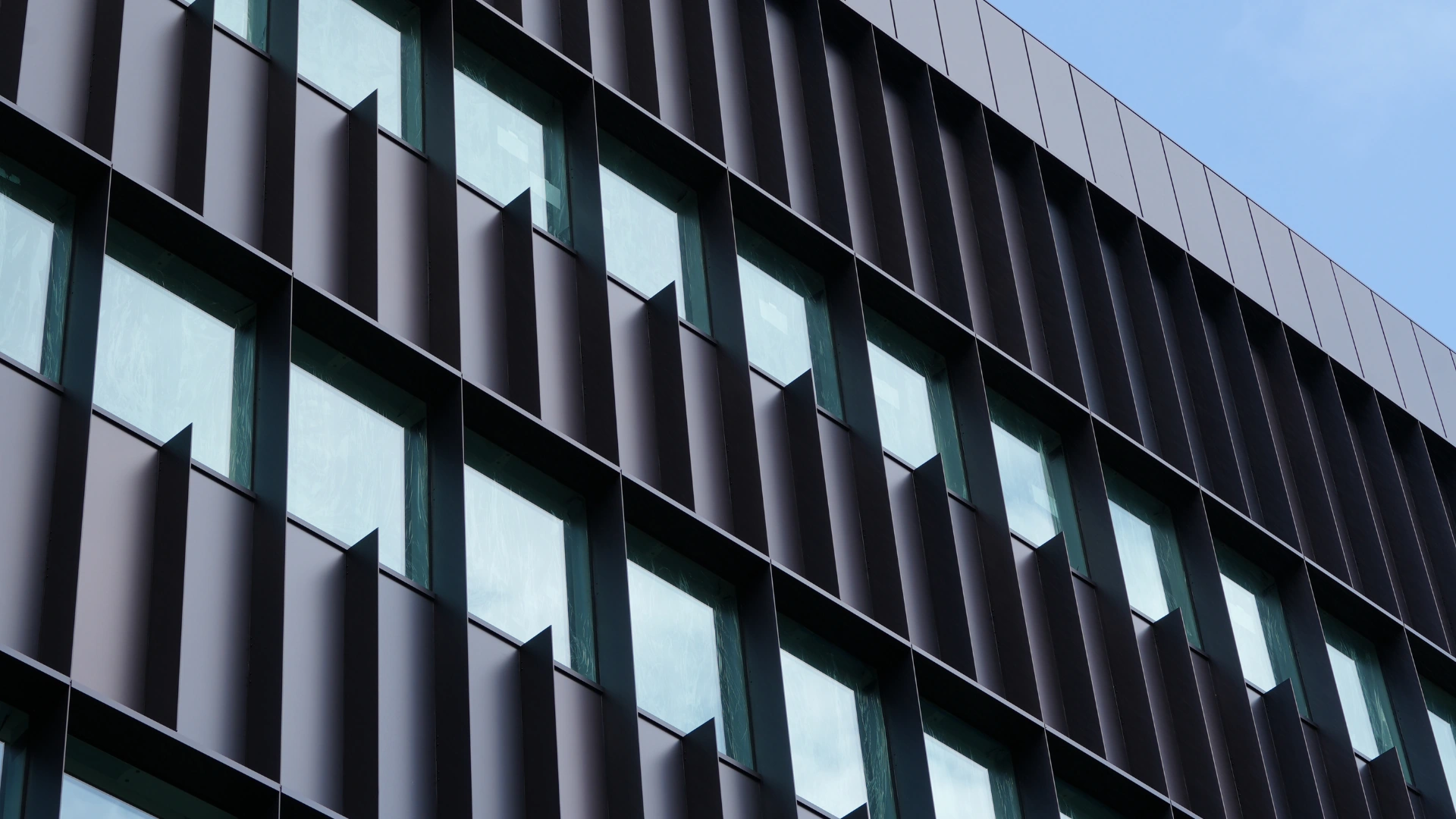 Modern building facade with repetitive windows and vertical dark panel blinds.