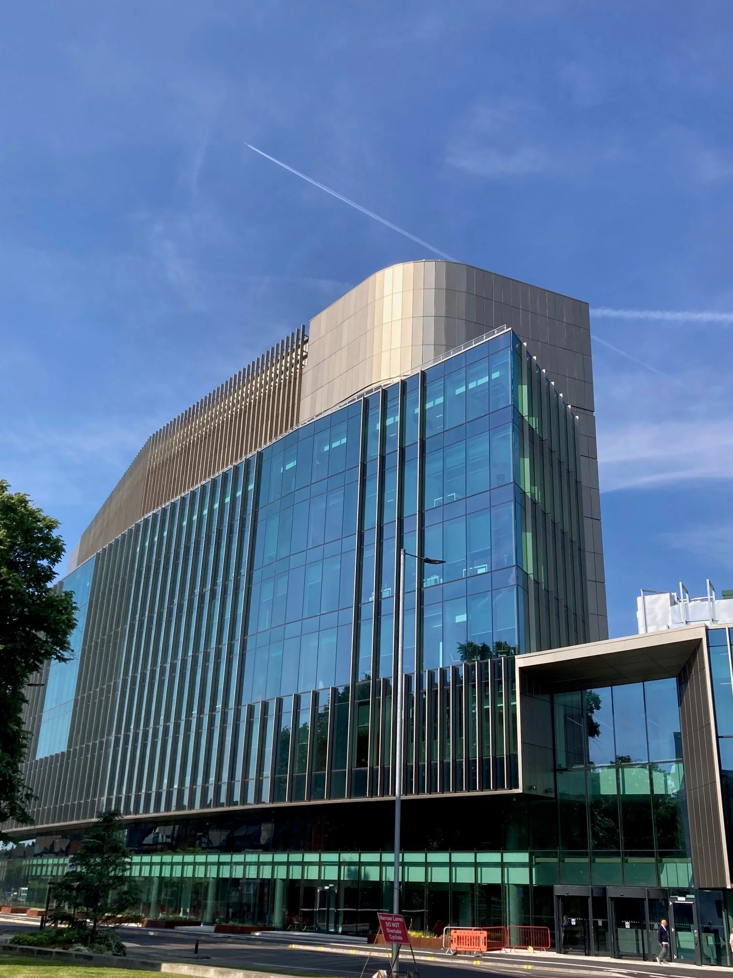 Modern glass building with vertical metal fins under a blue sky with contrails.