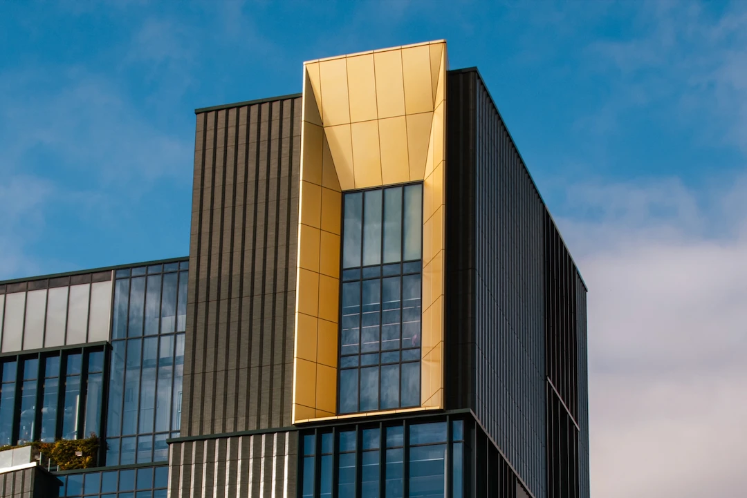 Modern black building with large windows and a gold anodised window frame under blue sky.