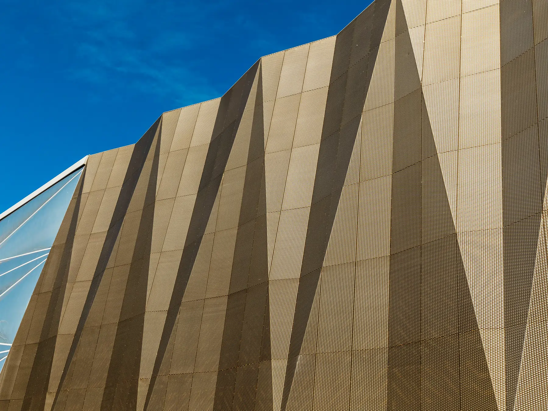 Close-up of a tan geometric patterned building facade against a clear blue sky.