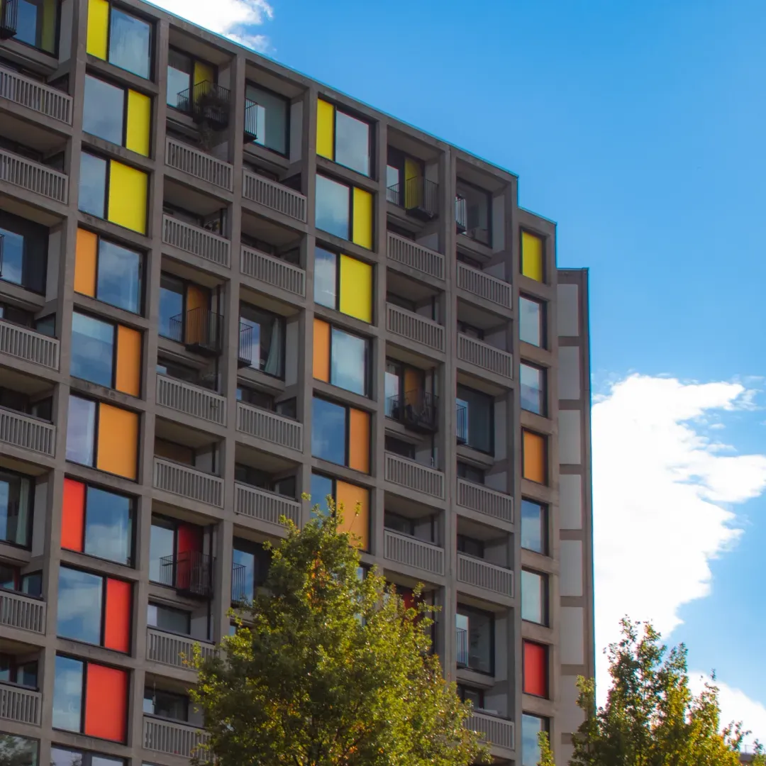 Apartment building facade with colorful red, orange, and yellow window panels under blue sky.