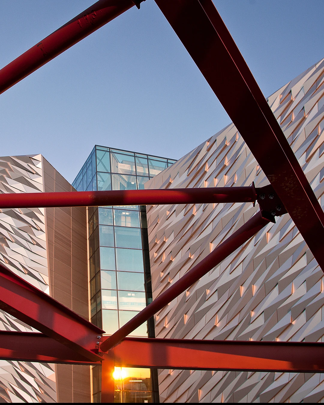 Modern building with textured walls viewed through red metal framework against a clear sky at sunset.