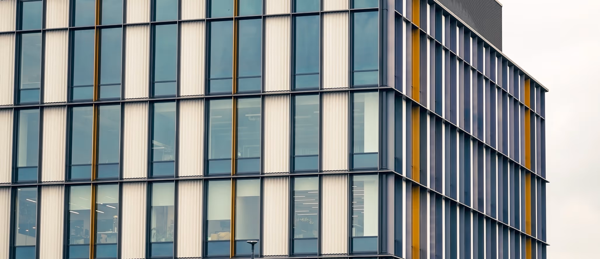 Exterior close-up of a modern office building with glass windows and vertical yellow and white panels.