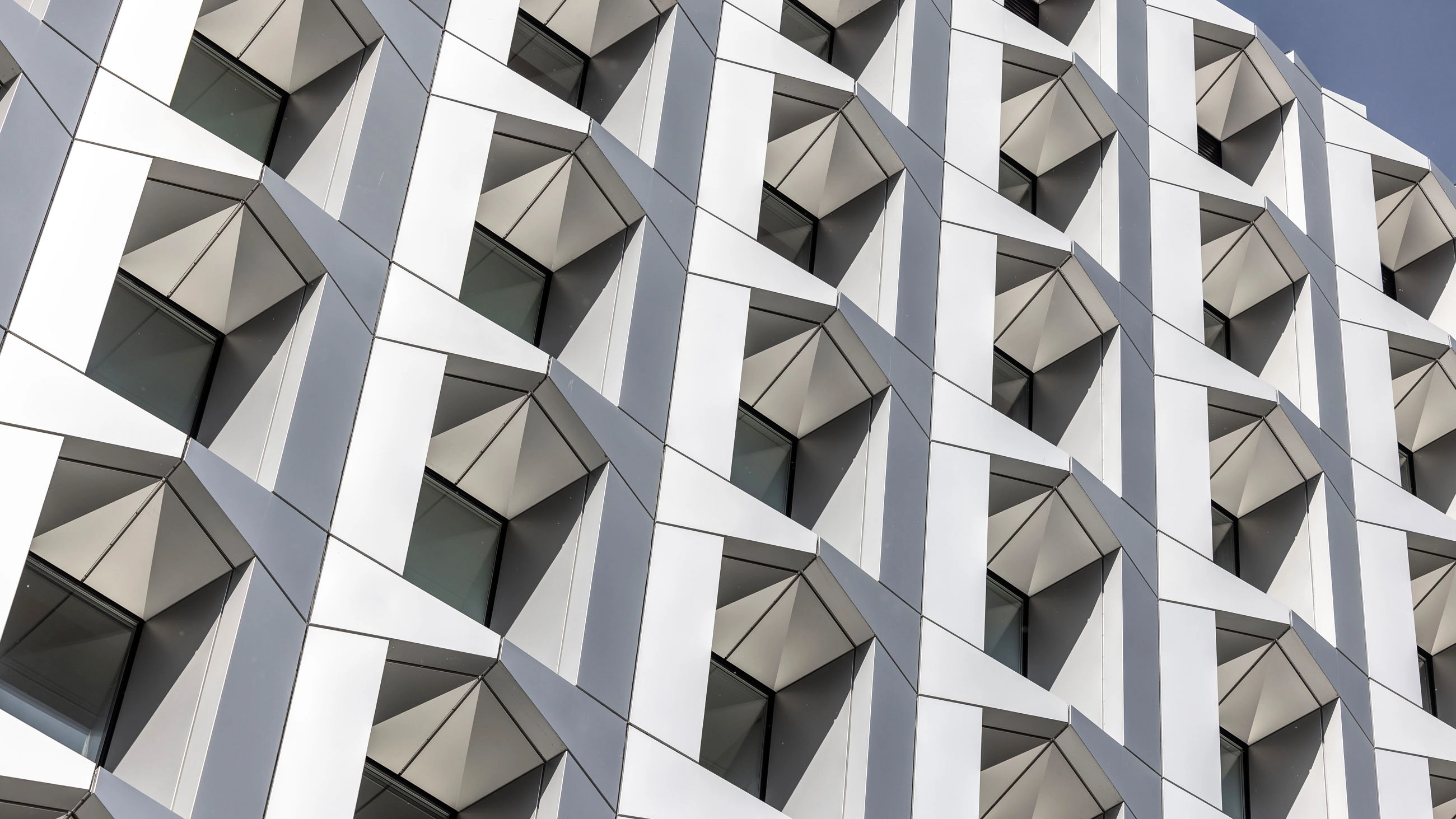 Modern building facade with geometric, angular white panels and dark windows arranged in a grid.