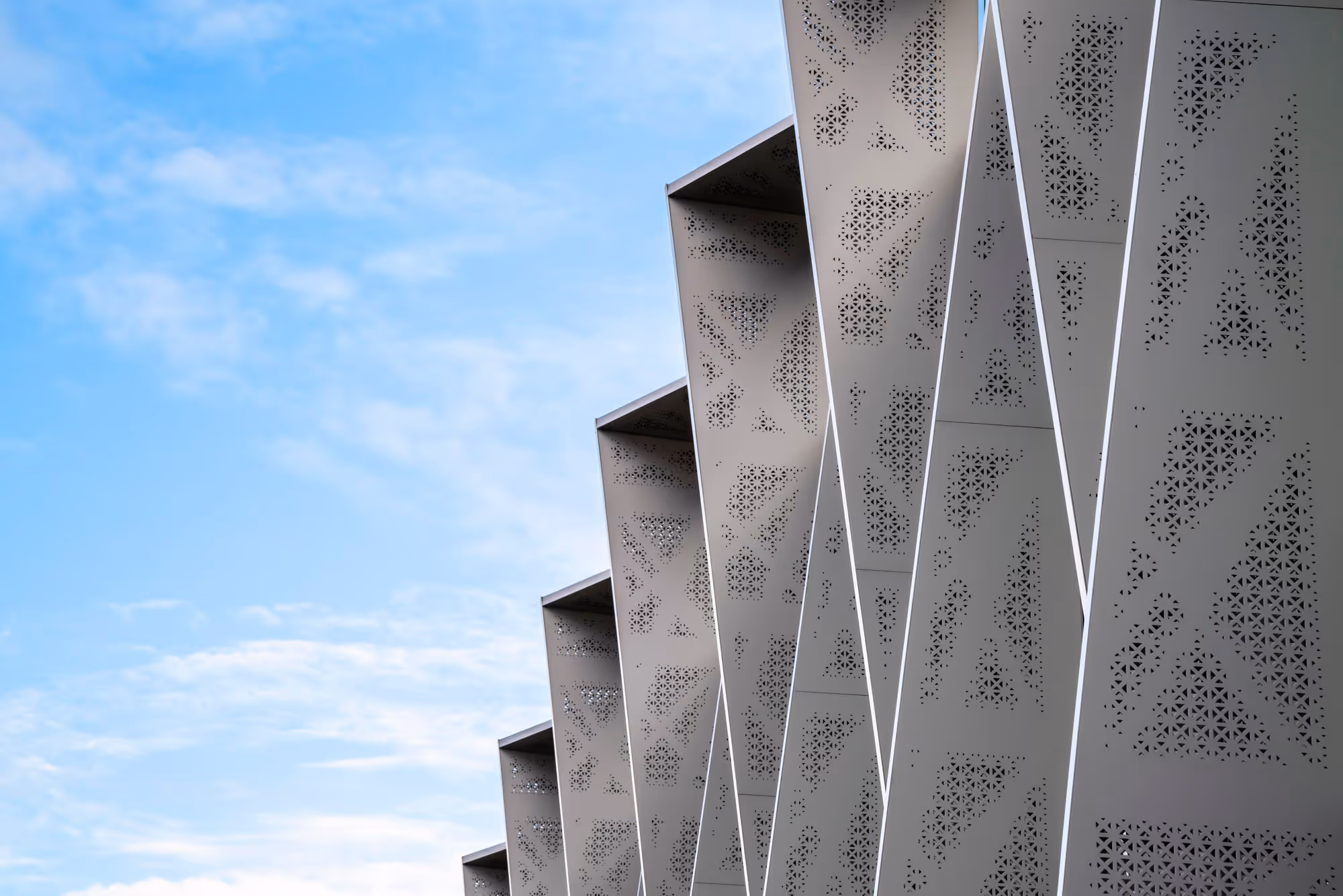 Close-up of a modern building facade with perforated metal panels against a blue sky.