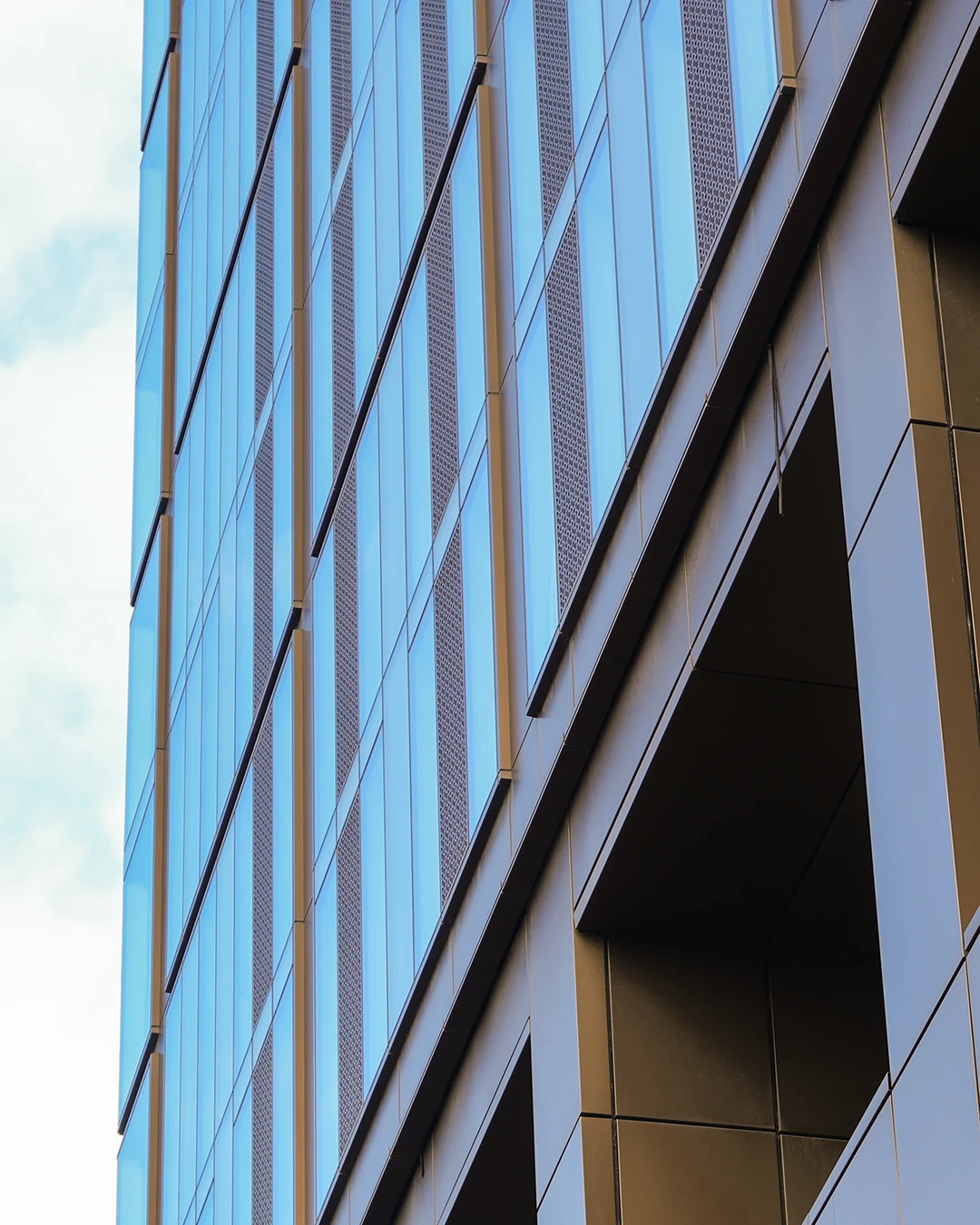Close-up angled view of modern building facade with blue glass windows and brown panels.