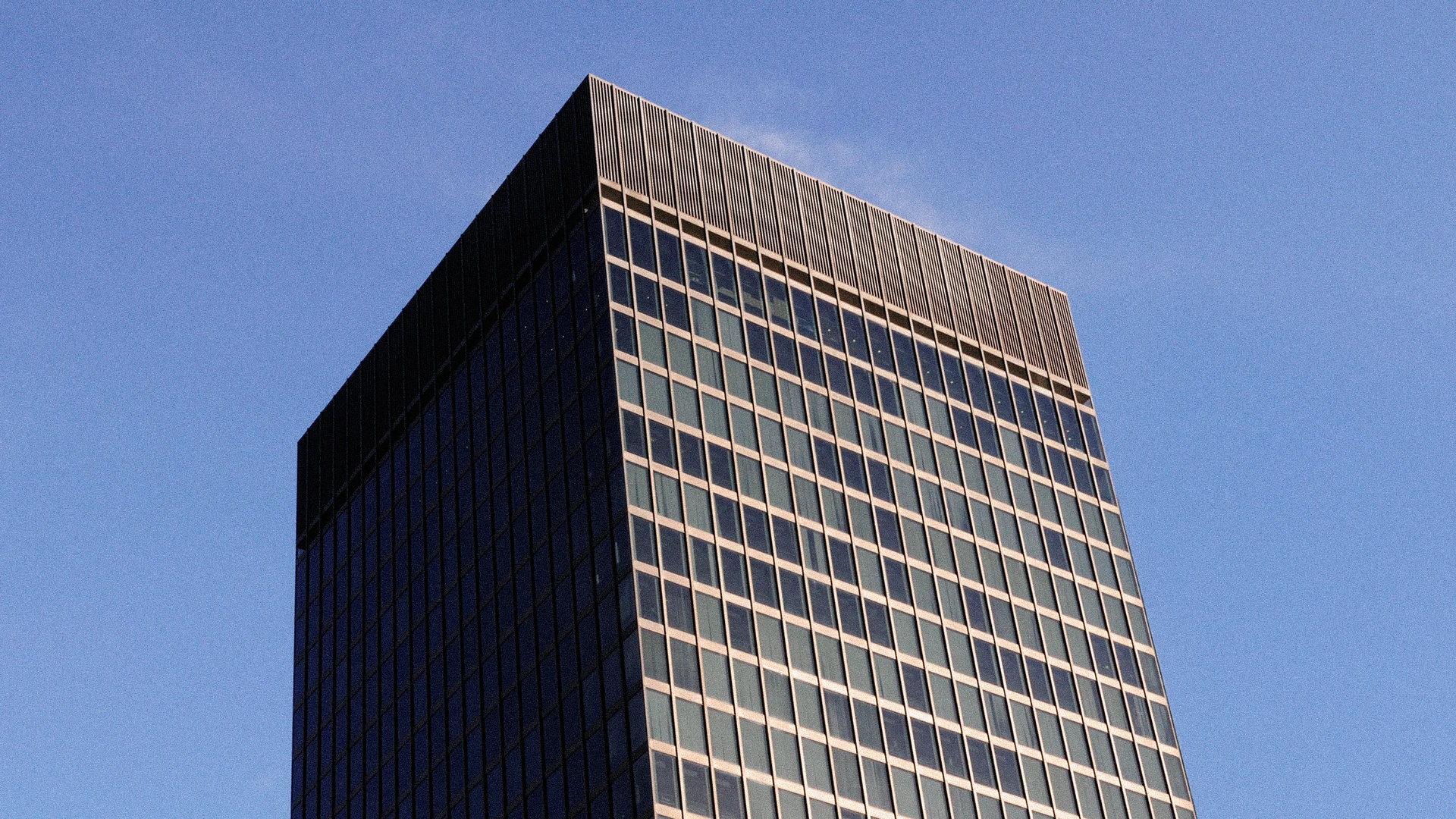 Modern glass office building with grid windows against a clear blue sky.