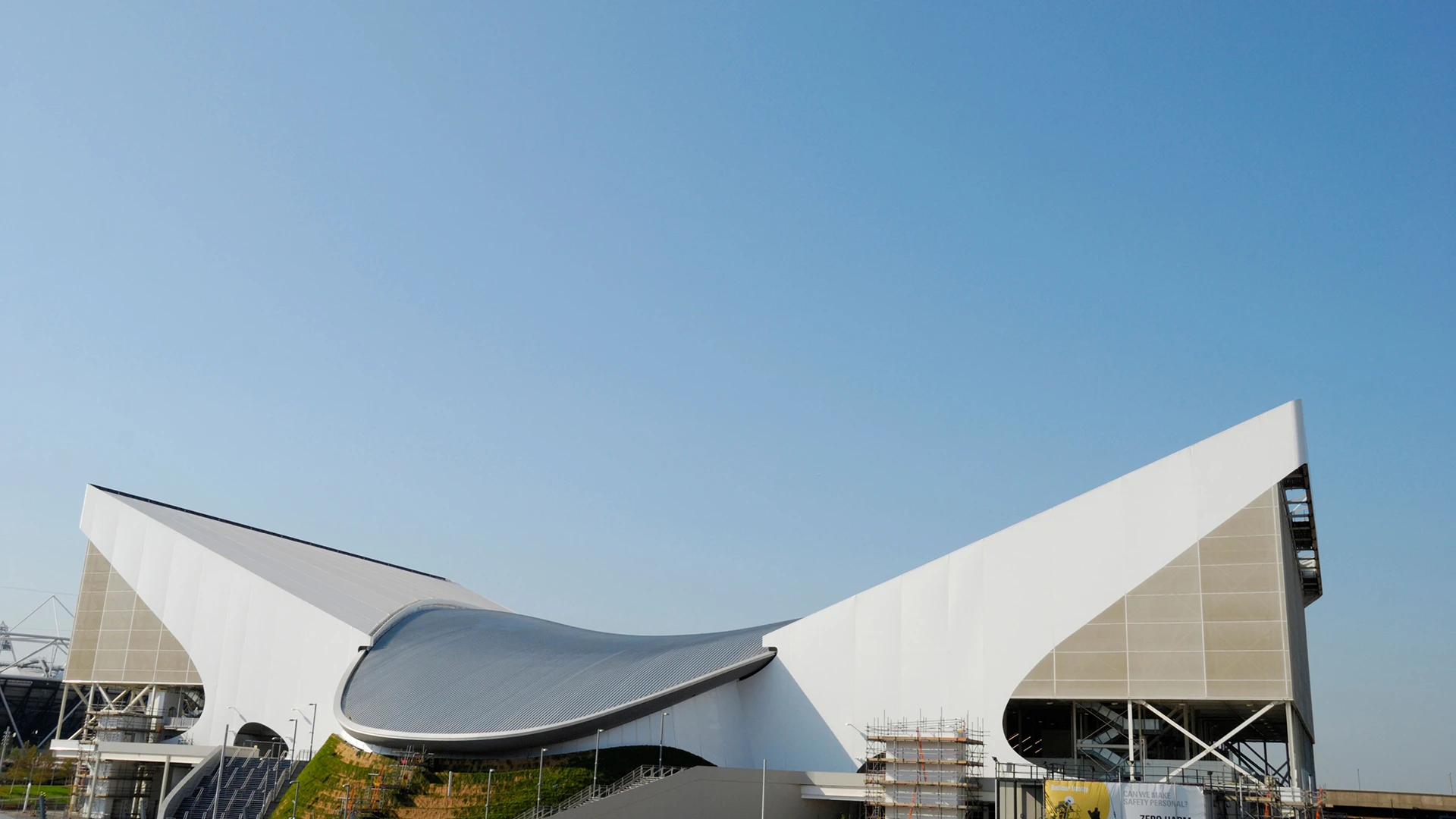 Modern London Aquatics Centre building with curved roof under clear blue sky.