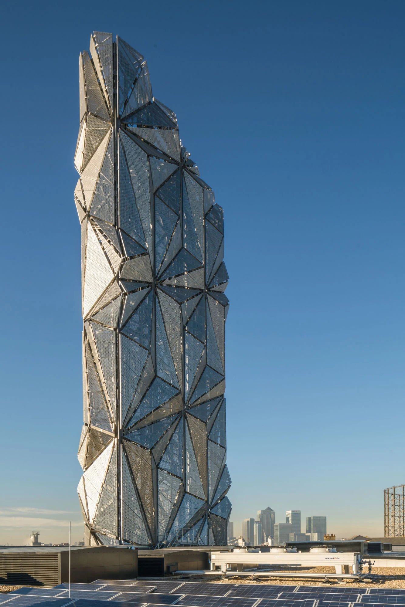Modern geometric solar panel tower on rooftop with city skyline and clear blue sky background.
