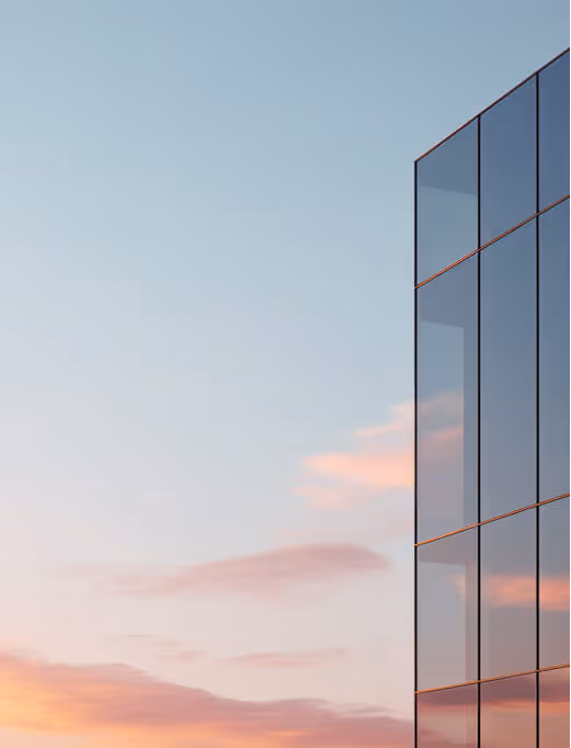 Façade vitrée d'un bâtiment moderne reflétant un ciel au coucher du soleil aux teintes roses et bleues.