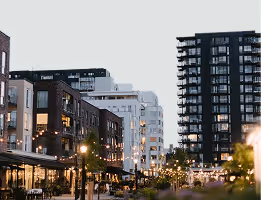 Vue urbaine avec des immeubles modernes et des lampadaires allumés en soirée.