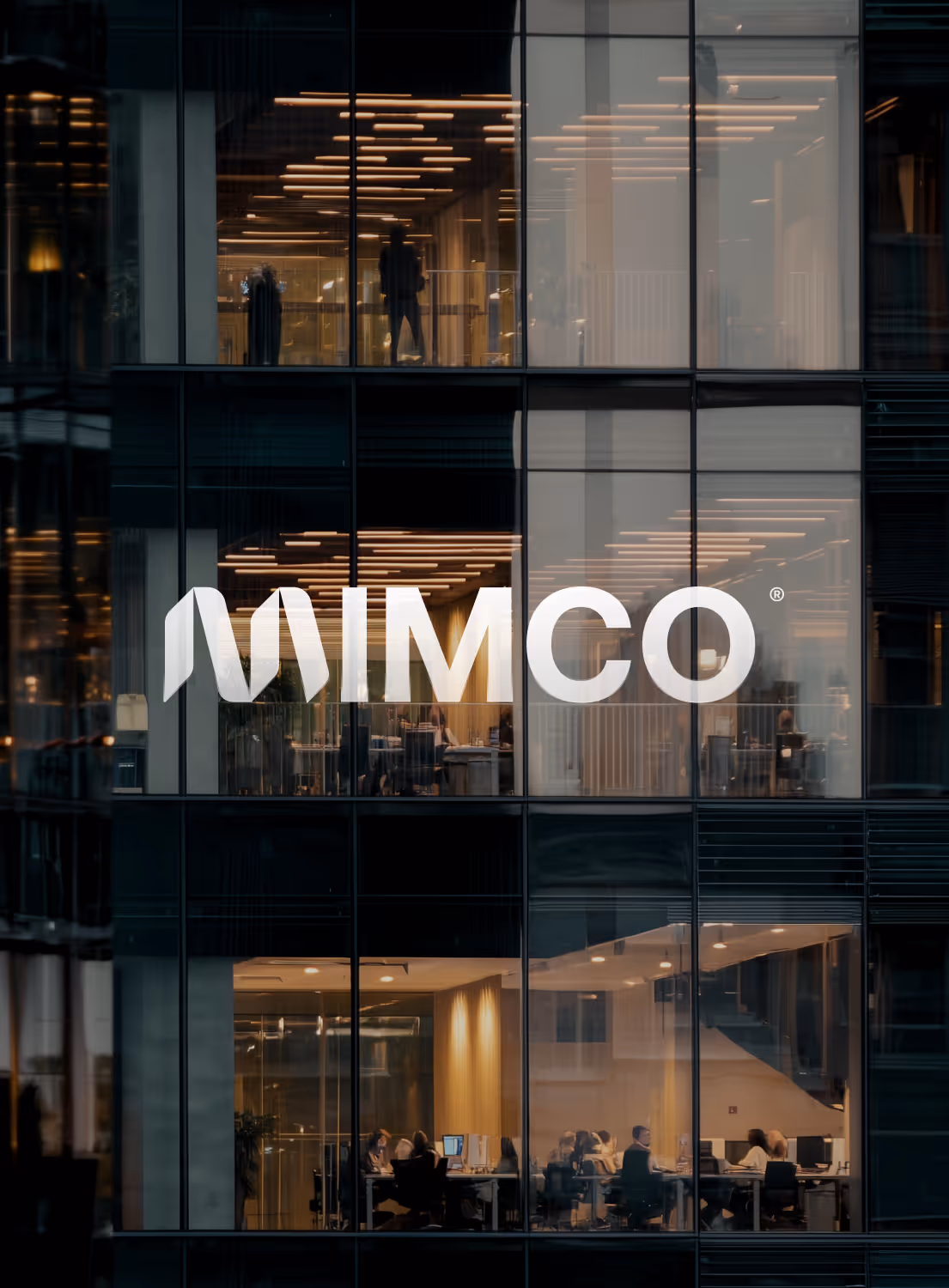 Vue d'un immeuble de bureaux moderne avec des personnes travaillant derrière de grandes baies vitrées et le logo MIMCO devant.