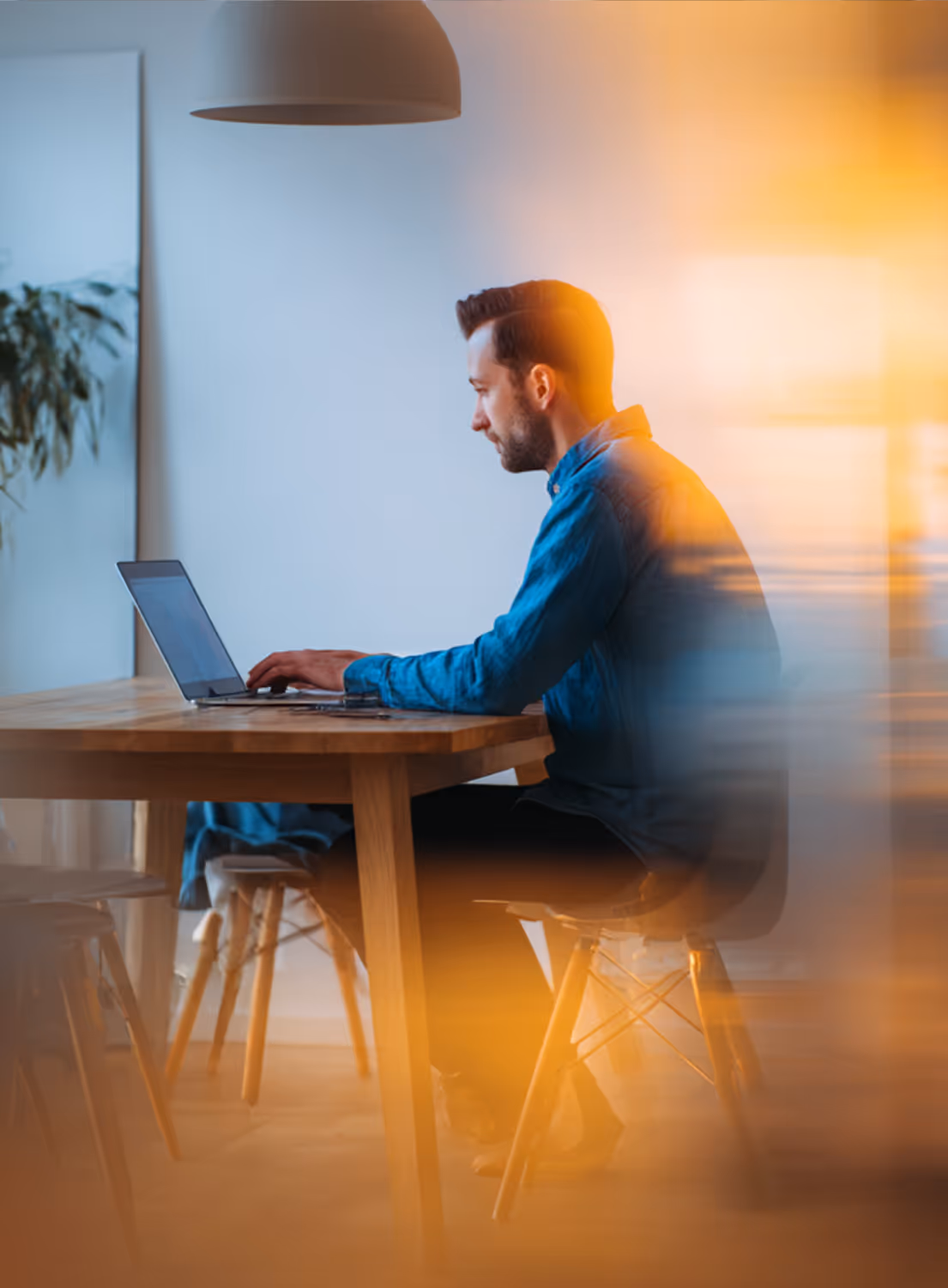Un homme assis à une table en bois travaille sur un ordinateur portable dans un espace intérieur moderne avec lumière tamisée.