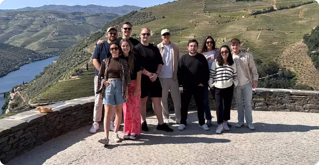 Group of nine people standing on a stone terrace overlooking a river and terraced hills under a clear sky.