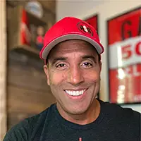 Smiling man wearing a red Deadpool cap and dark shirt indoors with blurred background.