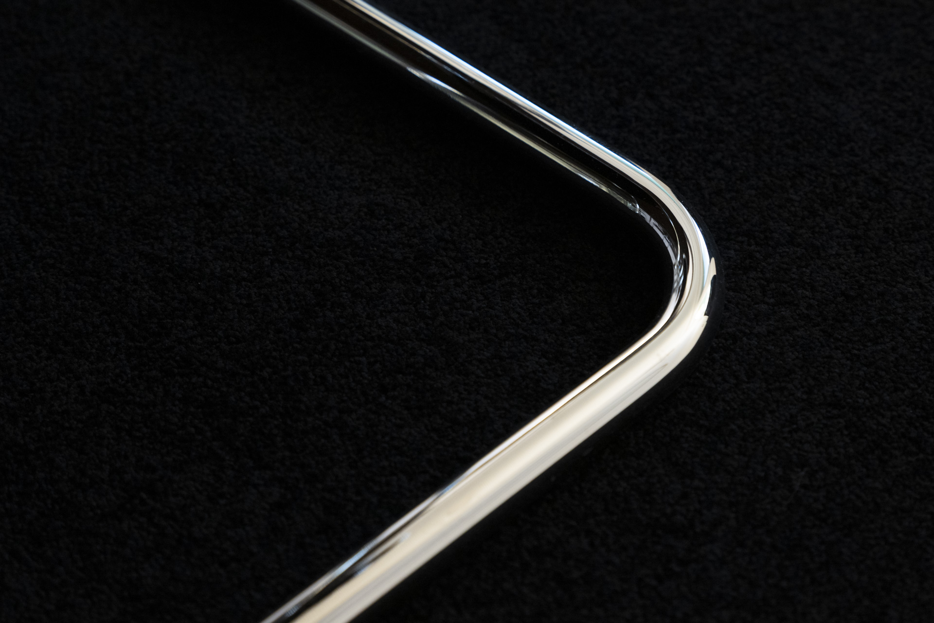 Close-up of a shiny metal object with a smooth, curved corner against a black textured background.
