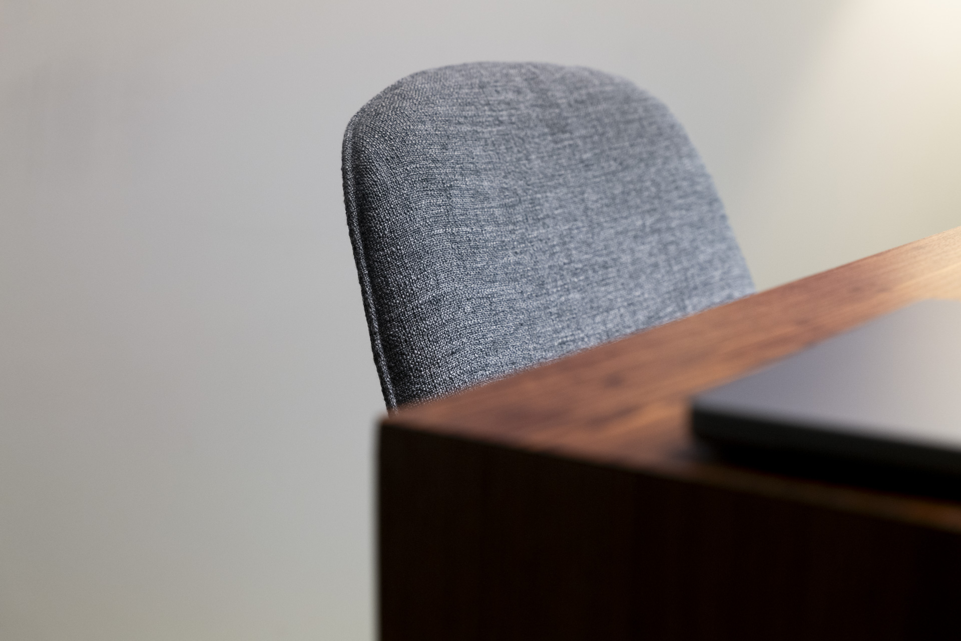 Close-up of a gray fabric chair back next to a wooden desk corner with a closed laptop.