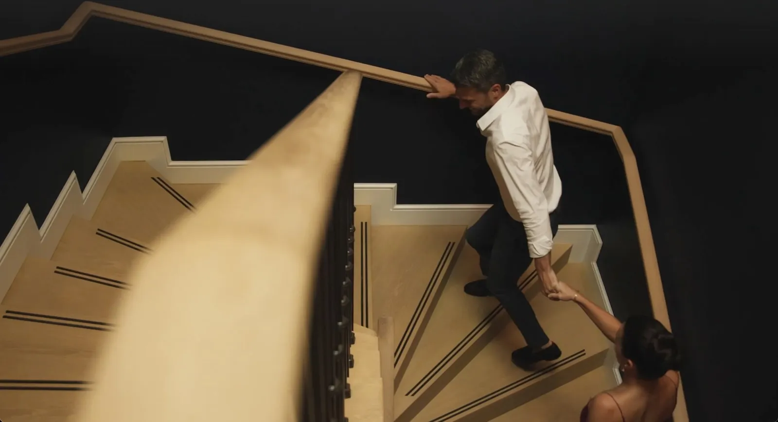 Homem e mulher de mãos dadas enquanto desciam escadas de madeira com paredes pretas.