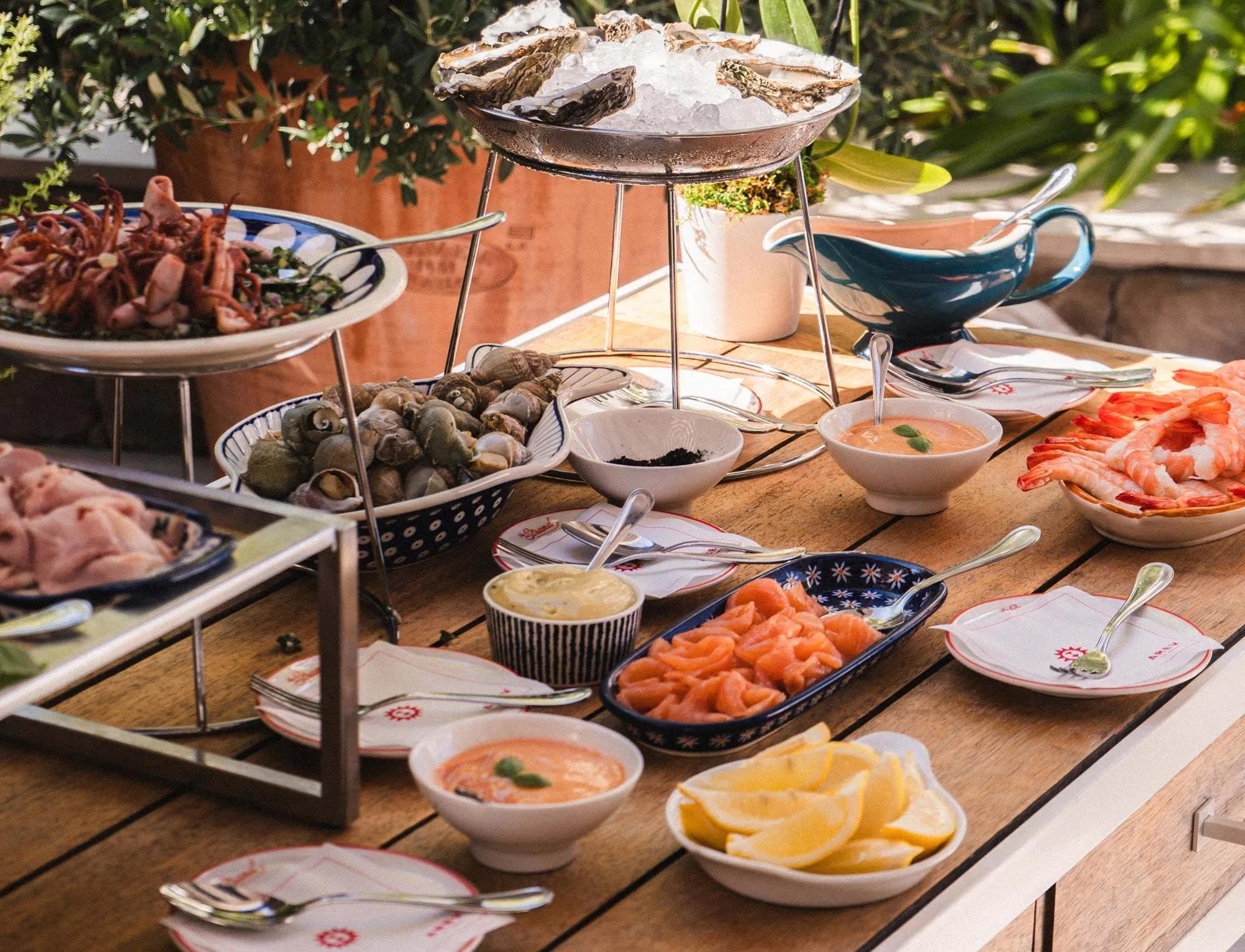 Gedeckter Tisch mit verschiedenen Fischgerichten, darunter Austern auf Eis, Garnelen, geräucherter Lachs, kleiner Tintenfisch und Meeresfrüchtesaucen.