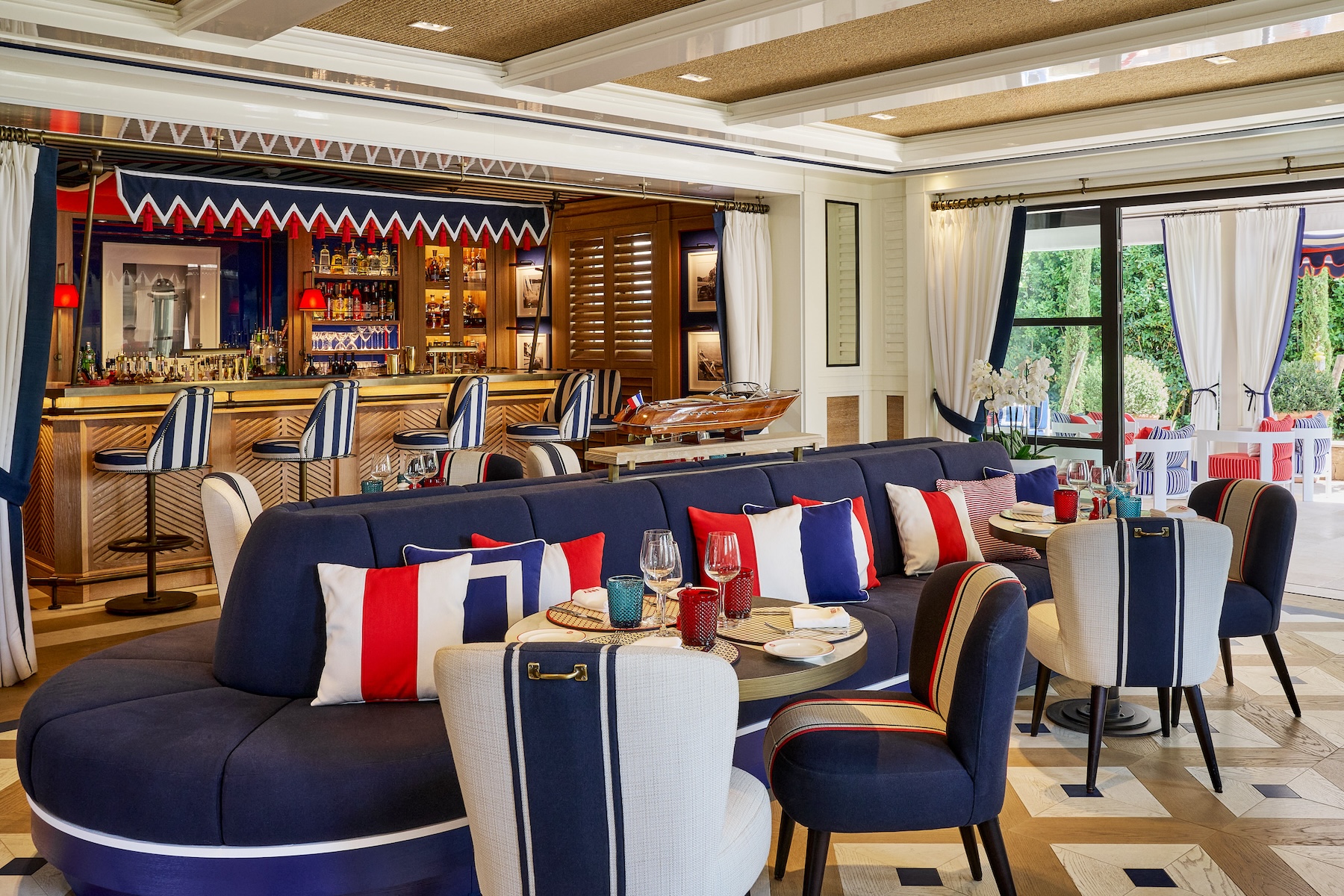 Lounge bar com temática náutica com assentos em azul marinho, almofadas às riscas, bancos de bar e um modelo de barco no balcão.