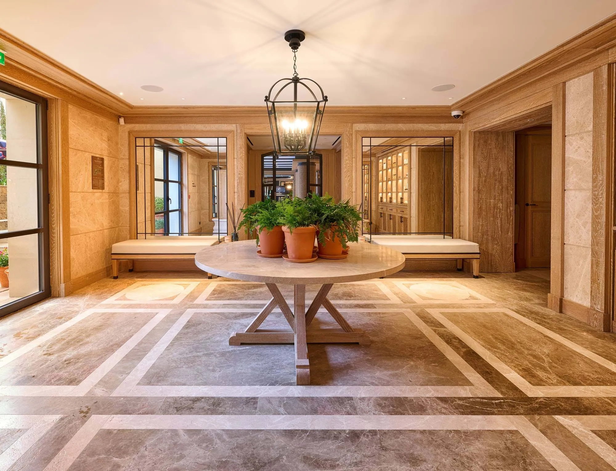 Die elegante Lobby verfügt über einen runden Marmortisch mit getopften Farnen, beigen gepolsterten Bänken, großen Spiegeln und warmen Holzvertäfelungen.