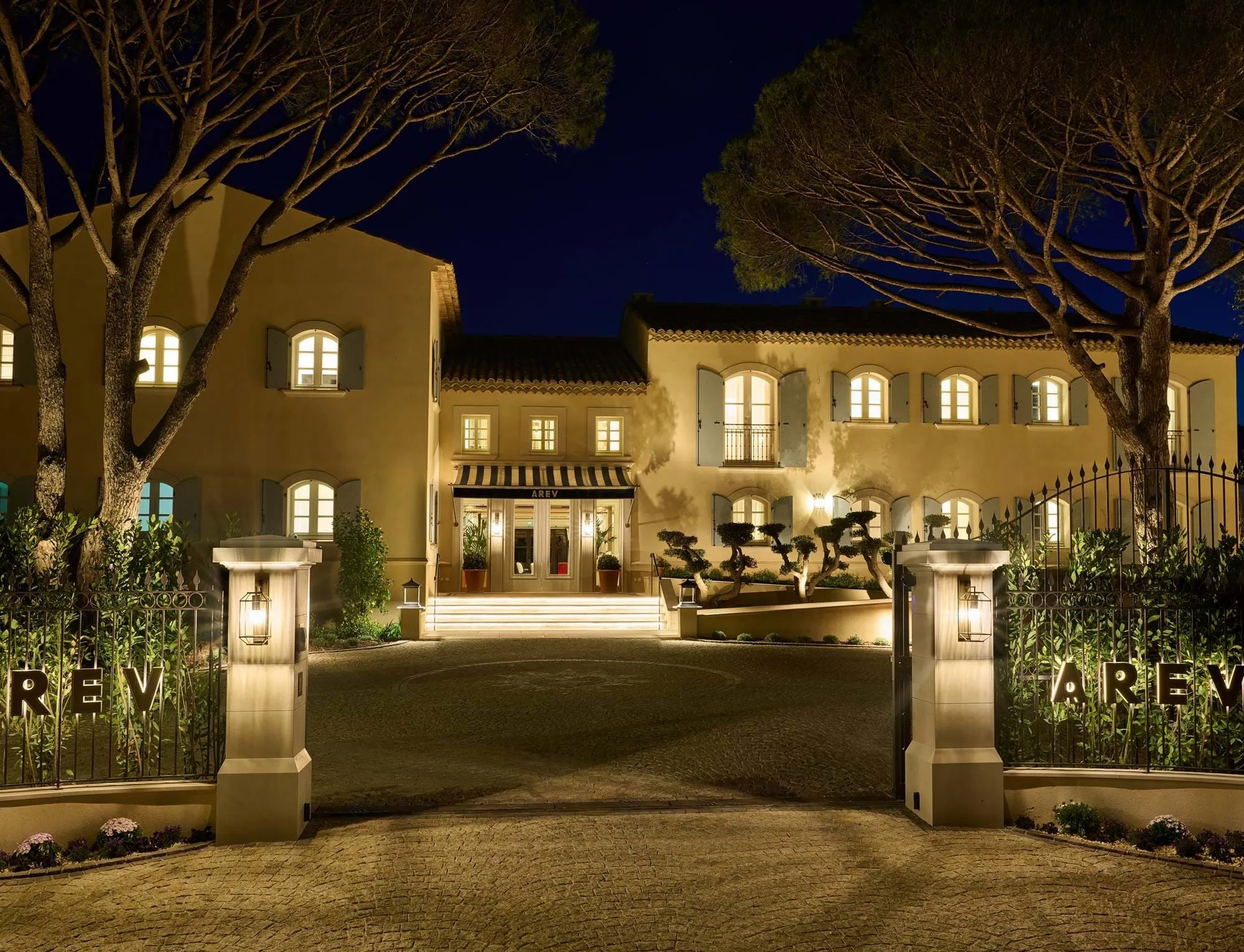 Entrée illuminée d'une grande villa élégante avec fenêtres éclairées et allée fermée la nuit.