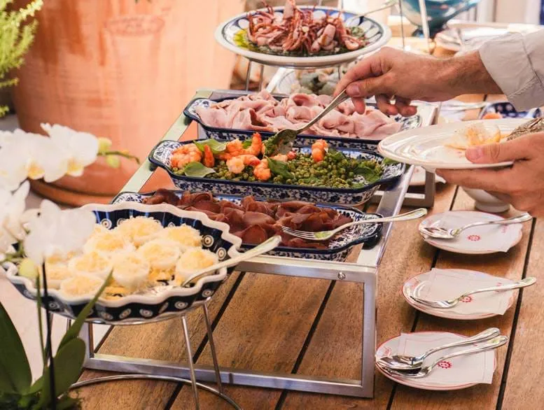 Servieren Sie Speisen von Hand aus Tabletts mit Garnelen, Gemüse und geschnittenem Fleisch an einem Buffettisch mit weißen Tellern und Löffeln.