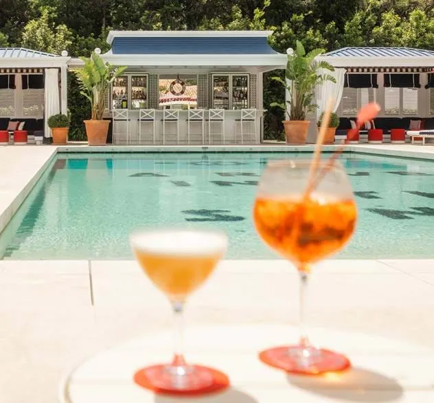 Dois cocktails coloridos junto à luxuosa piscina do AREV Hotel Saint-Tropez com o bar exterior ao fundo.