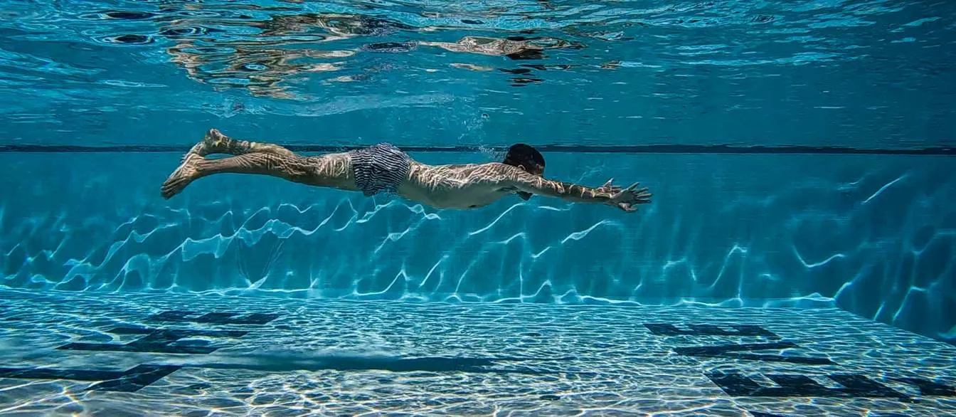 Mann schwimmt unter Wasser im türkisfarbenen Pool des AREV Hotels in Saint-Tropez.