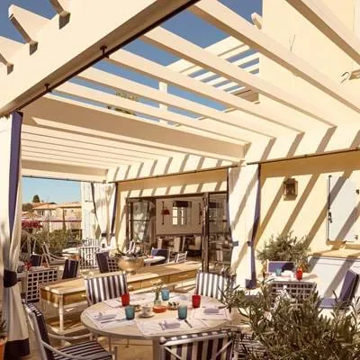 Terraço ensolarado sob uma pérgola de madeira com uma mesa de jantar no hotel AREV em Saint-Tropez.