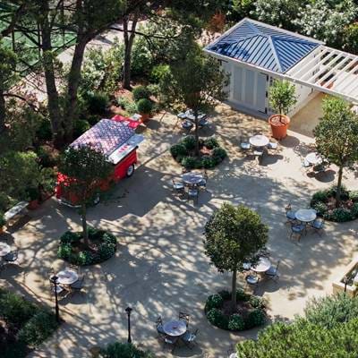 Pátio exterior sombreado no hotel AREV em Saint-Tropez com assentos no jardim e um food truck vermelho vintage.