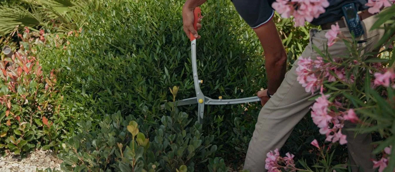 Ein Gärtner, der sich um das üppige Grün und die rosa Blumen in den Gärten des AREV Hotel Saint-Tropez kümmert.