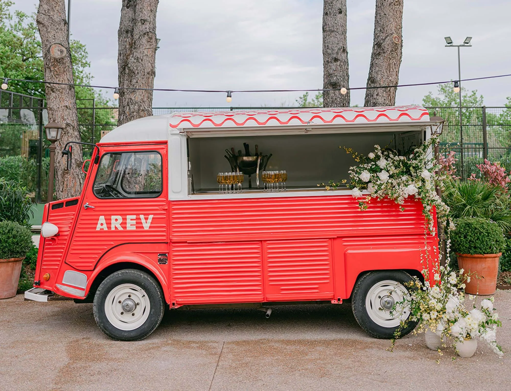 Food truck vermelho vintage adornado com flores brancas estacionado nos jardins do AREV Hotel Saint-Tropez.
