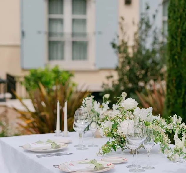 Elegante mesa de casamento com linho branco, velas afiladas e arranjos florais brancos exuberantes no AREV Hotel Saint-Tropez.