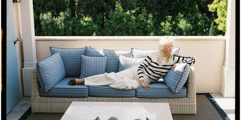 Uma mulher relaxando num confortável sofá exterior azul num terraço privado no hotel AREV em Saint-Tropez.